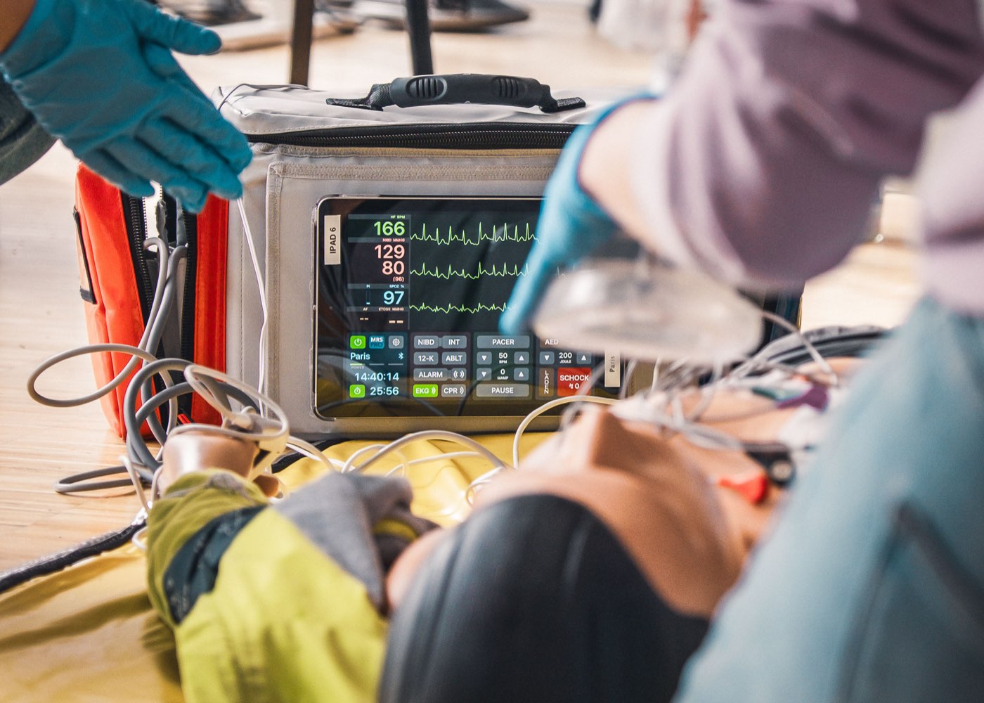 Monitor-Defibrillator mit Vitalwerten, im Vordergrund die Beatmung einer Übungspuppe