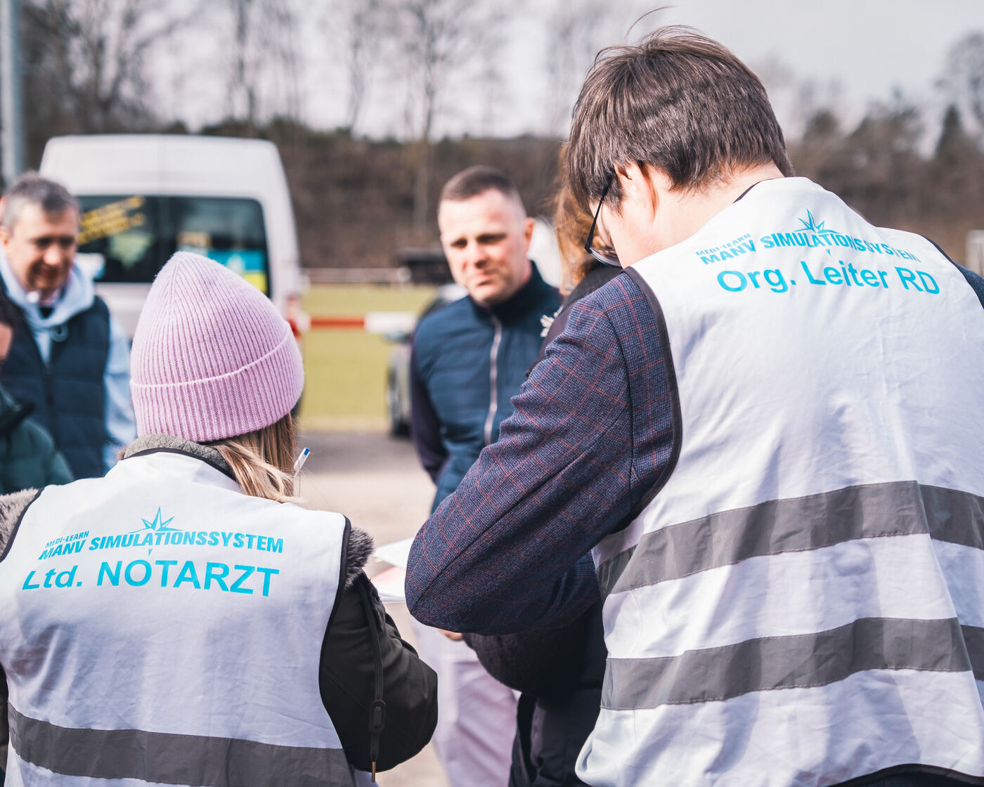 Teilnehmende in Warnwesten mit der Aufschrift „Ltd. Notarzt“ und „Org. Leiter RD“ bei einer Übung im Freien