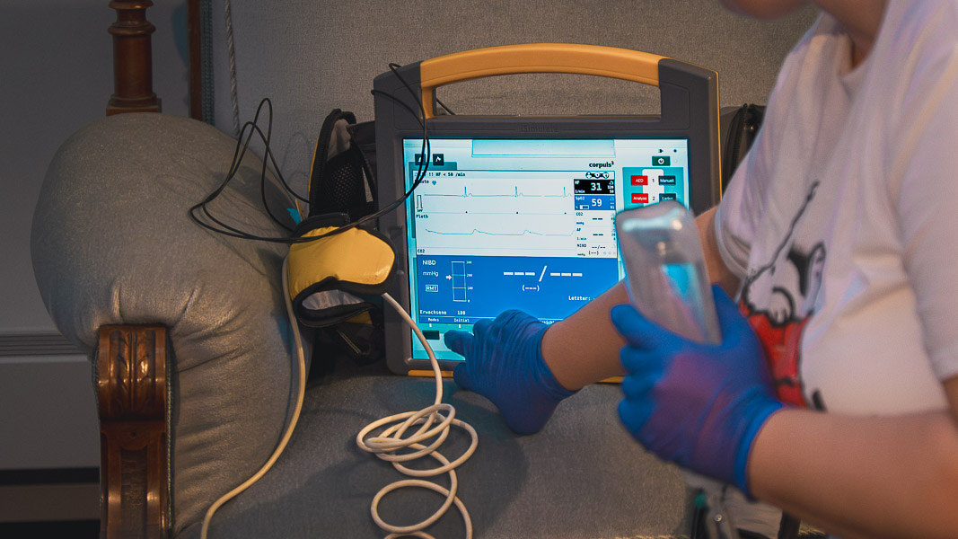 Eine behandschuhte Hand bedient den Monitor eines Defibrillators mit EKG-Anzeige