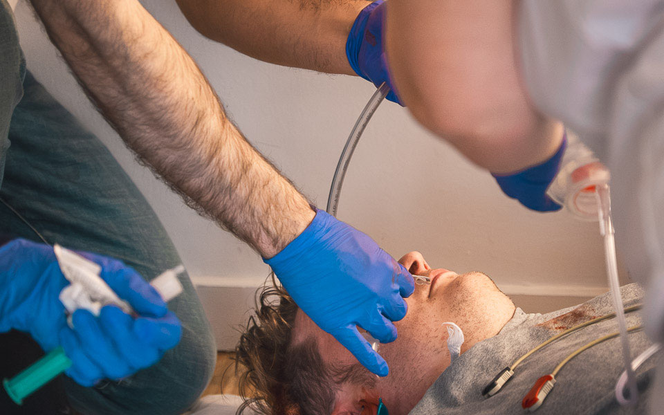 Ein Teilnehmer hält einem liegenden Simulationspatienten eine Sauerstoffmaske vor das Gesicht