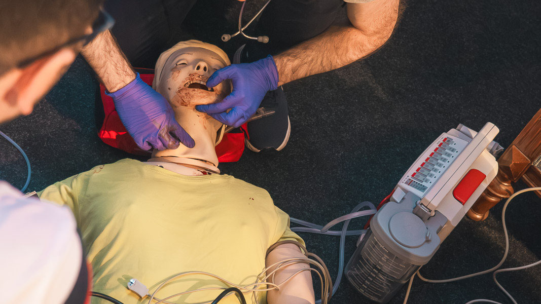 Teilnehmende sichern bei einer Simulationspuppe die Atemwege, daneben ein Defibrillator