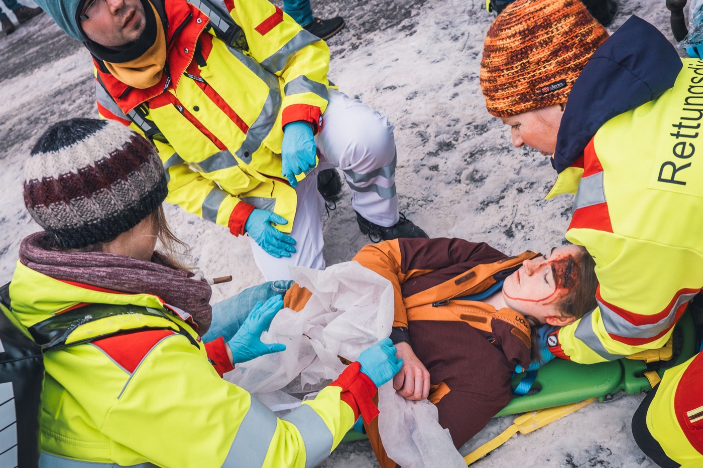Einsatzkräfte in Warnkleidung versorgen bei einer Übung im Schnee eine am Boden liegende Person