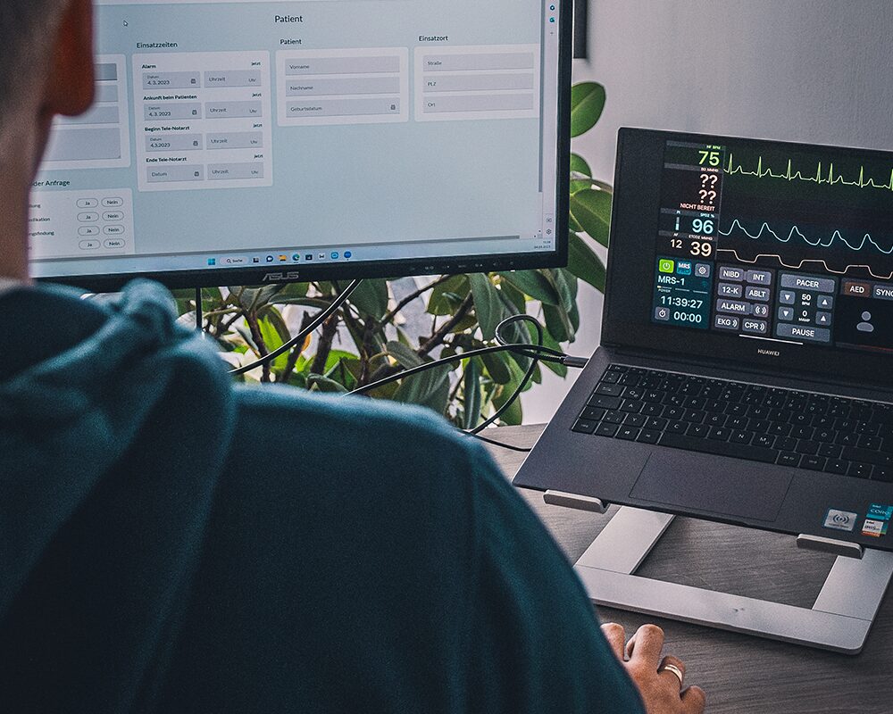Blick über die Schulter auf einen Telenotarzt-Arbeitsplatz mit mehreren Monitoren